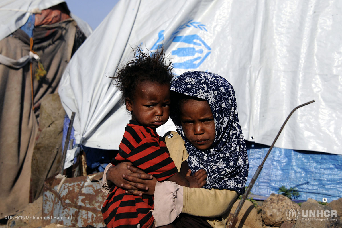 A girl carries her brother outside their tent at the Dharawan settlement.