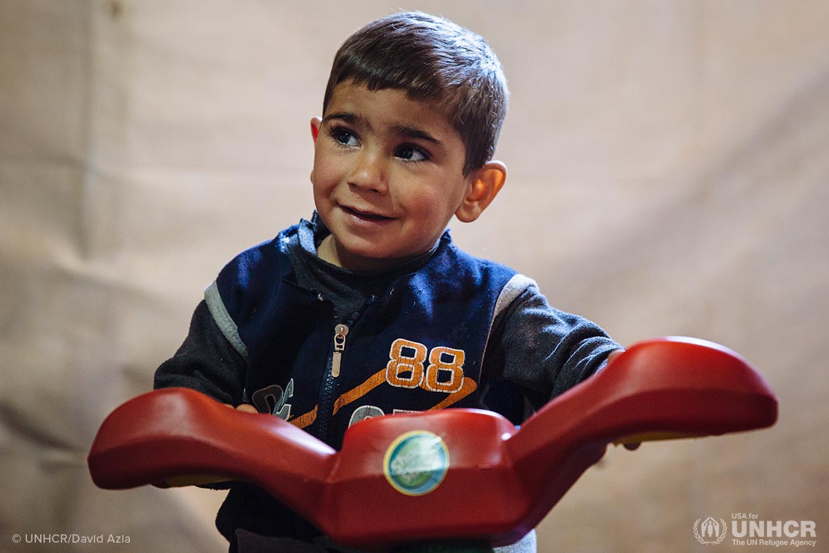 Syrian refugees Yehya, 3, sits on a tricycle in his family's shelter at an informal settlement near Terbol in the Bekaa Valley