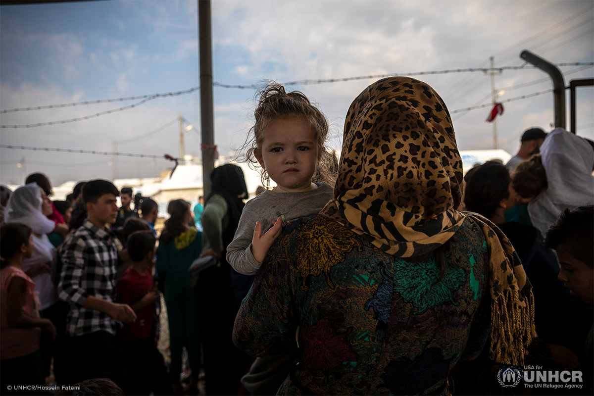 displaced syrian child being held by mother looks at camera