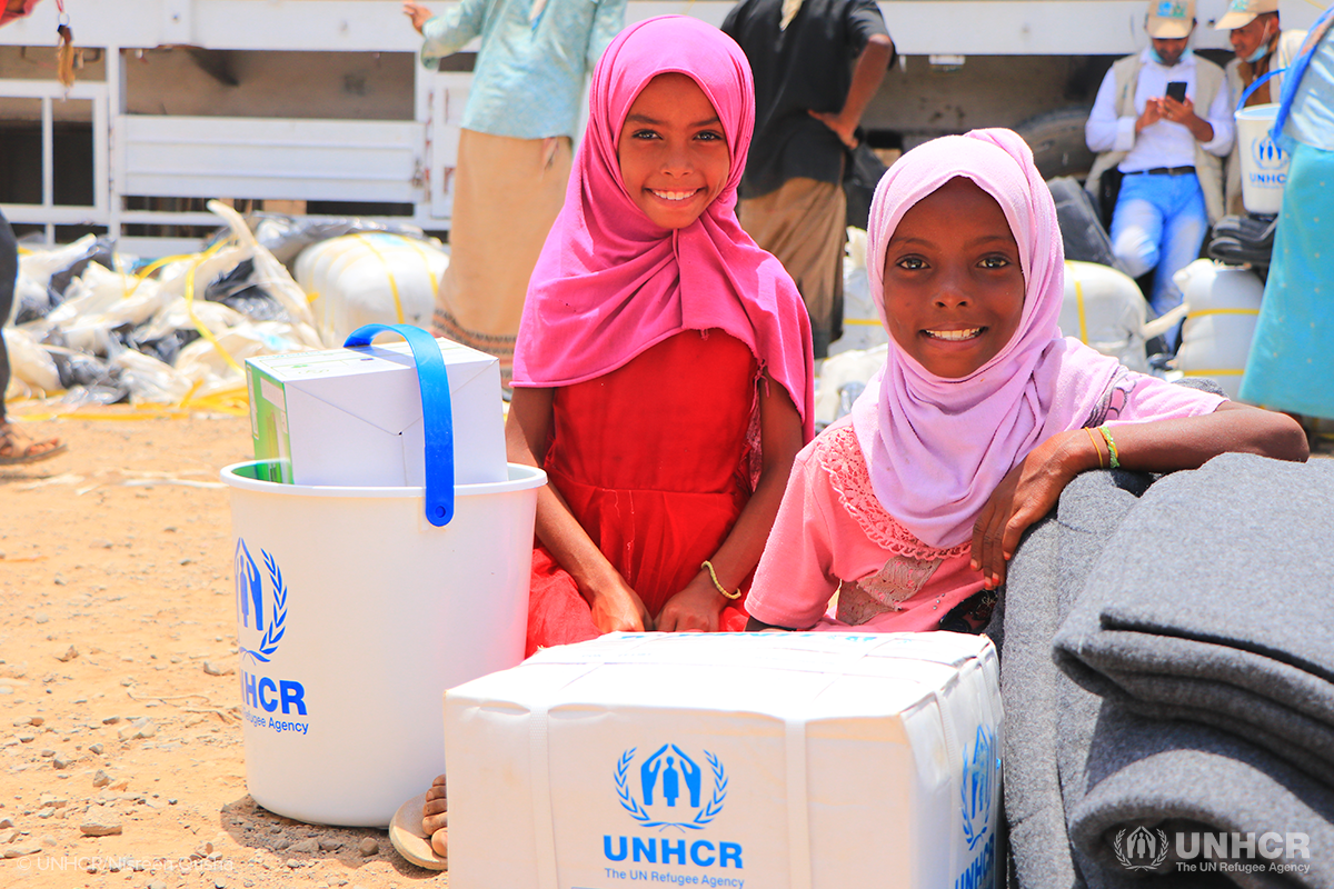displaced Yemeni girls smiling with UNHCR boxes