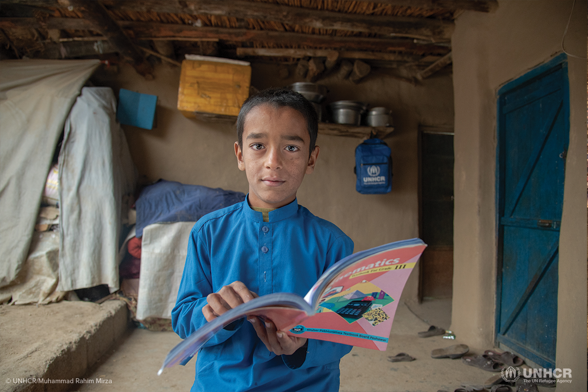 afghan refugee child yasir holding up his homework book