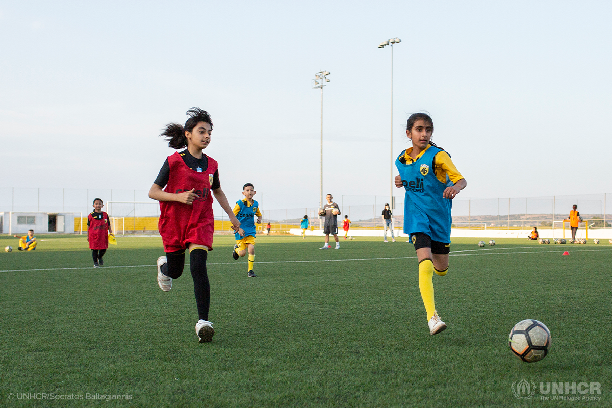 two refugee girls in the aek athens football club chase a soccer ball