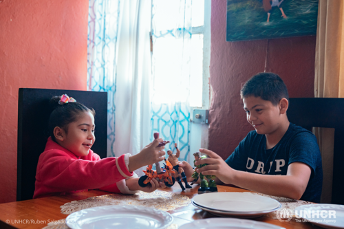 Eleven-year-old refugee Javier and his sister Nelly wait at the kitchen table for breakfast to be served by their mother Dania.