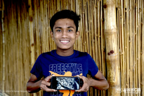 Hasson holds a mobile phone showing the photograph of him taken by Kevin Frayer in 2017, soon after he arrived to Bangladesh with his family.