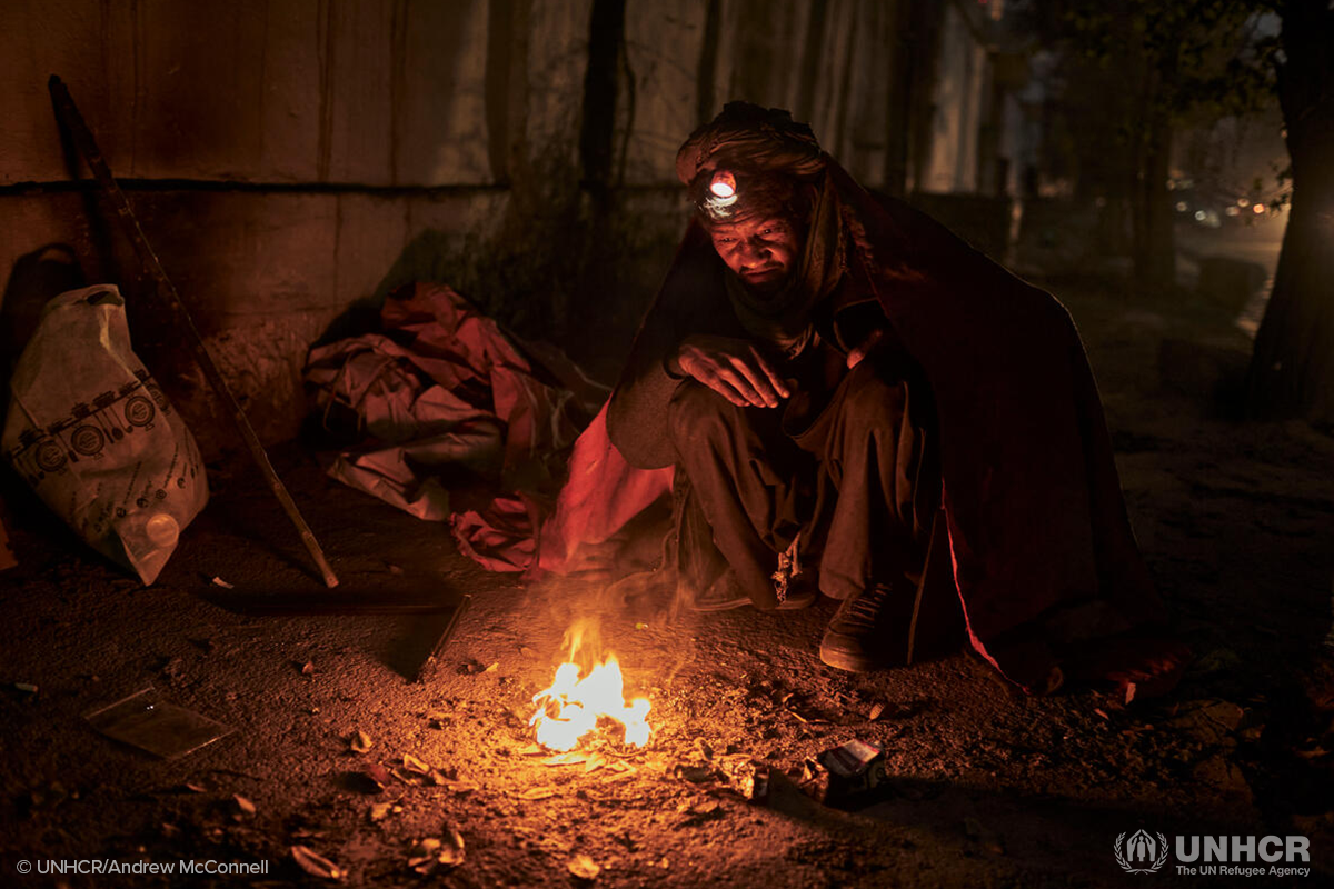 Displaced Afghan man sits next to a fire outside