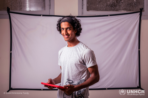 Adham holds a red tablet while smiling.
