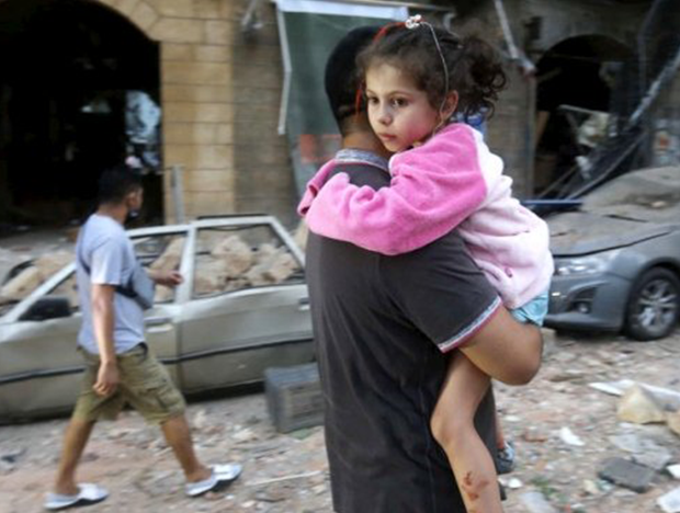 A man carries an injured child to safety following a massive blast in the port of beirut lebanon