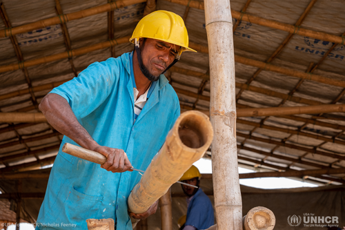 Noorul, a Rohingya refugee from Myanmar, uses a machete to work bamboo poles.