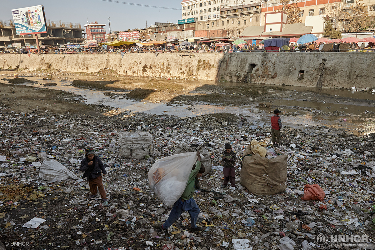 displaced Afghan children collect trash near a river