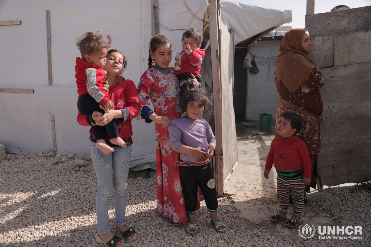A group of 6 Syrian children holding onto one another, spending time in the outdoor areas at an informal refugee settlement.