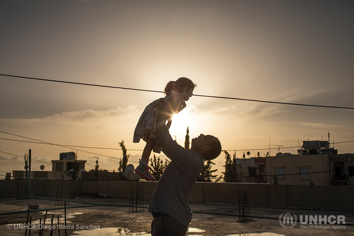 syrian refugee father holds up his daughter