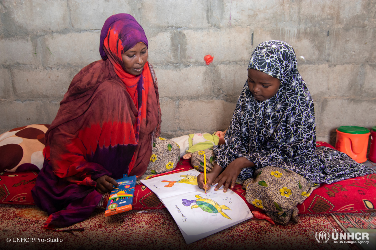 Najma doing homework with her foster mother in Kharaz refugee camp